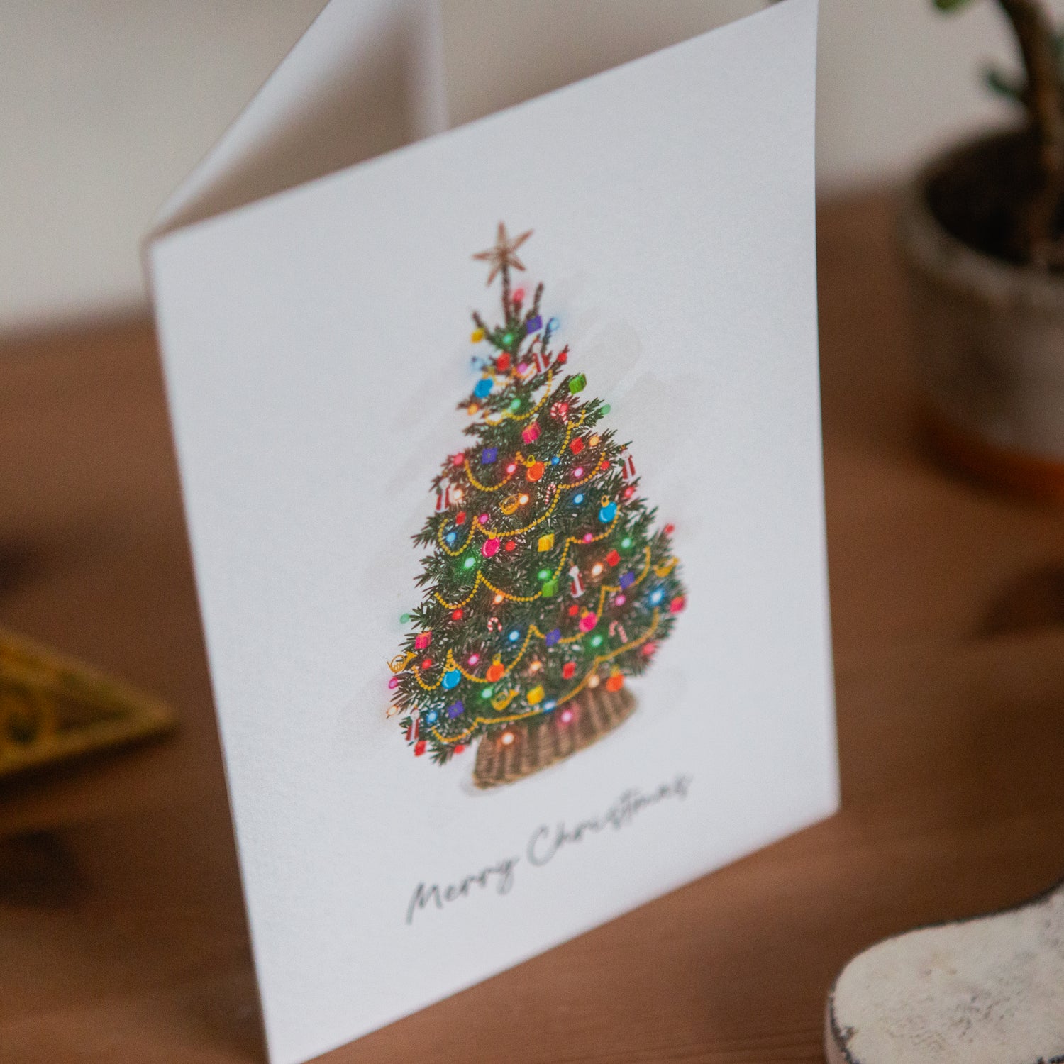 Greeting card with a Christmas tree illustration and 'Merry Christmas' text on a wooden surface.