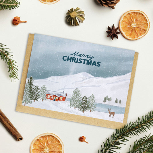 Christmas card with snowy landscape and cabin, surrounded by festive decorations on a white background.